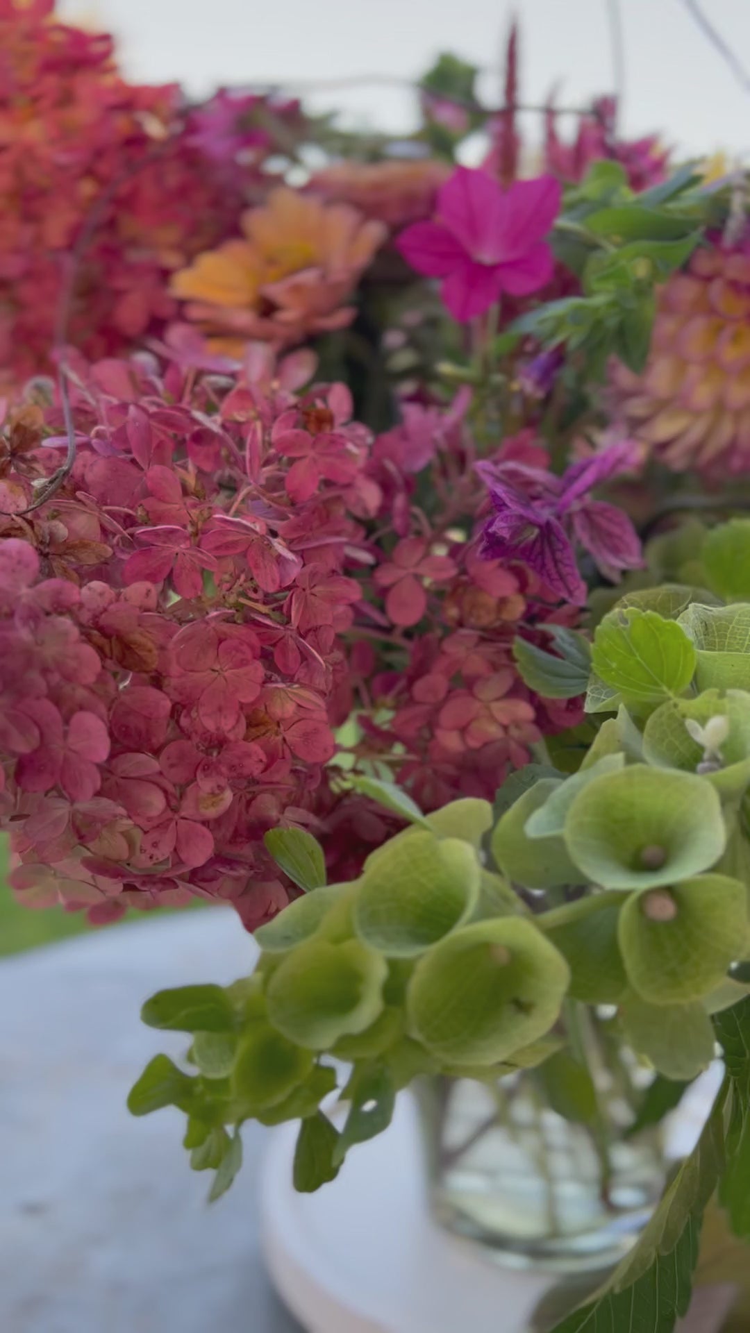 Video showcasing summer blooms of pink, peach, green, and purple in a centerpiece arrangement.